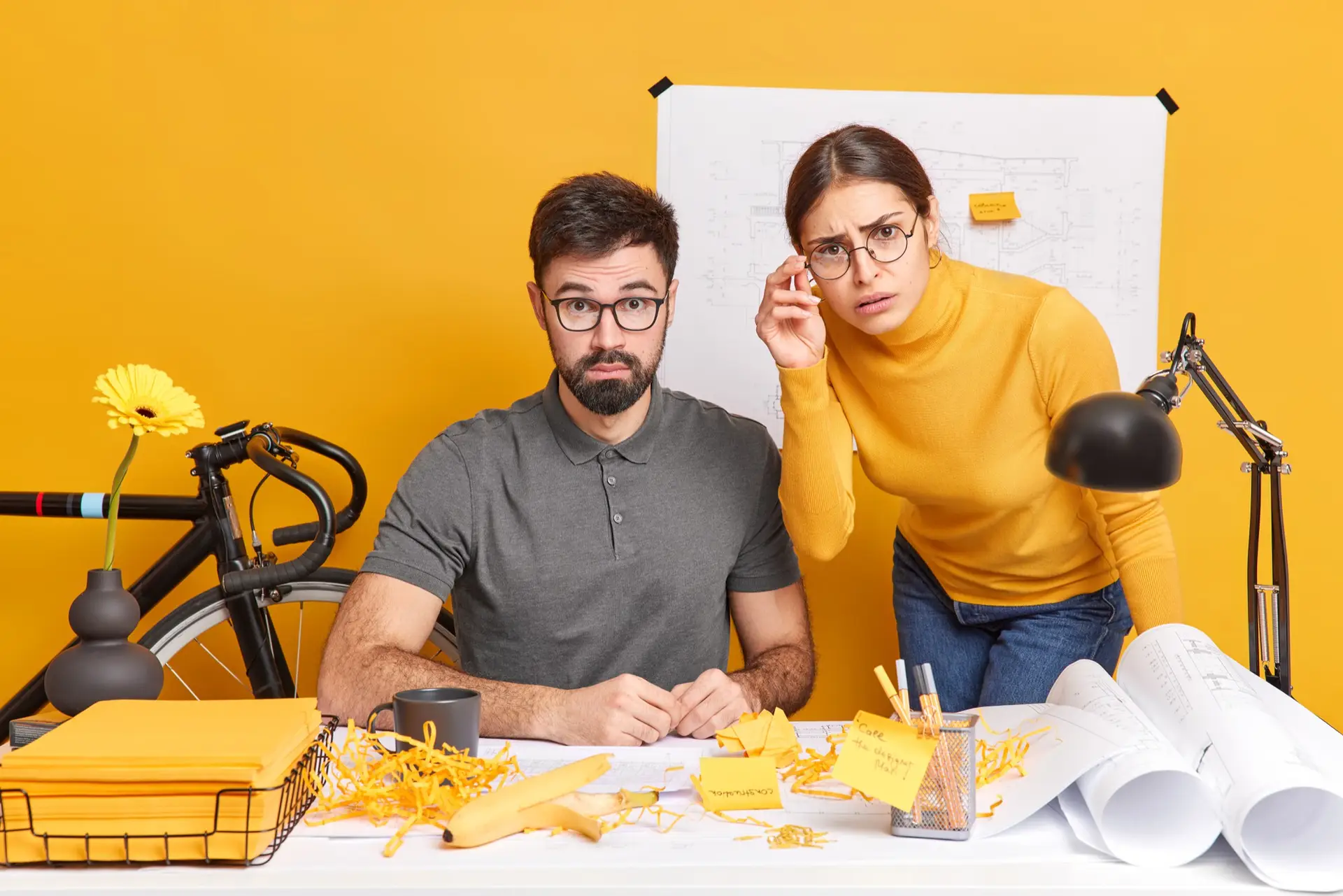 Two people puzzled at messy desk setup.