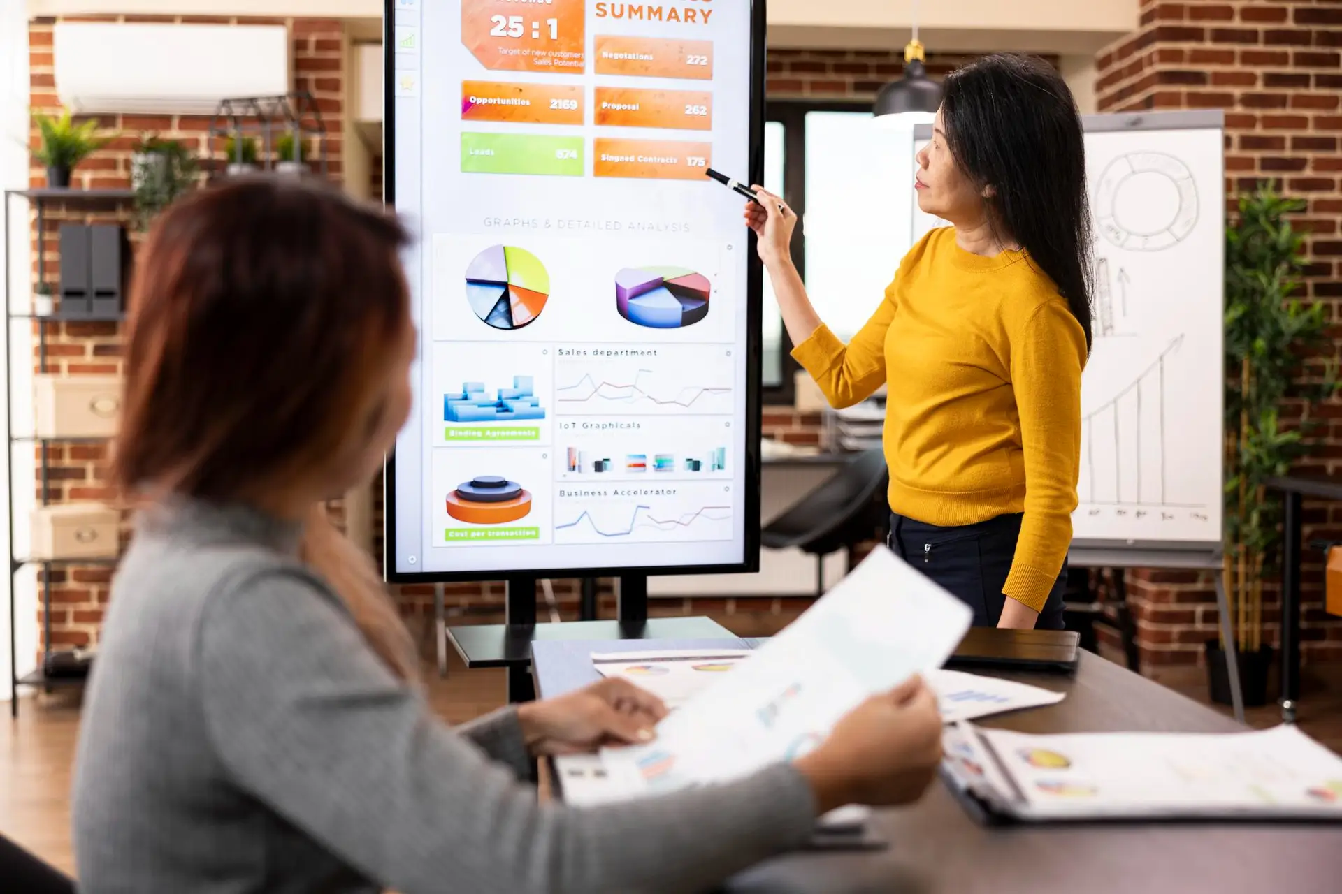Woman presenting data on monitor in meeting room.
